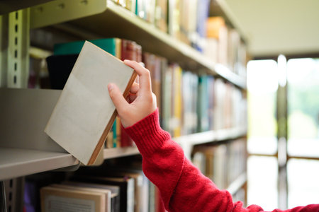 Female hand pulling book from bookshelf in public library in university, college or high school..