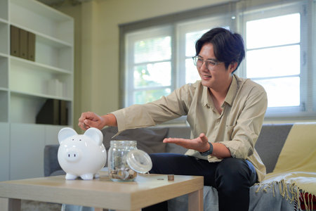 a man putting coins into a piggy bank at home, saving money for future goals, casual wear,.の写真素材