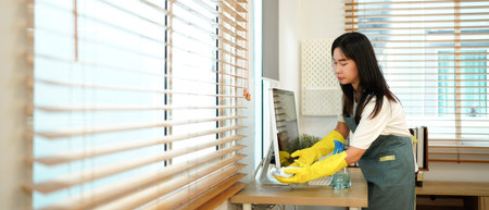 Female worker of cleaning service wiping computer screen in office.