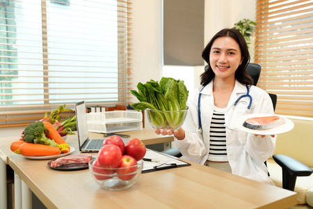 Smiling female nutritionist holding a fresh vegetable and salmon while sitting at desk with vegetables and fruits. Healthy food and diet planning concept.の写真素材