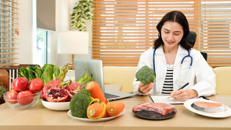 Professional nutritionist plans healthy diet with fresh vegetables and fruits while writing notes in a bright modern office setting..の写真素材