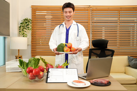 Smiling male nutritionist holding a fresh vegetable while stand at desk with vegetables and fruits. Healthy food and diet planning concept.の写真素材