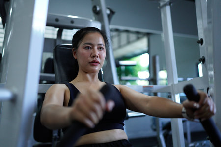 Asian fitness woman working out on chest press machine at gym. Healthy lifestyle and strength training.の写真素材