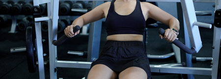 Asian fitness woman working out on chest press machine at gym. Healthy lifestyle and strength...
