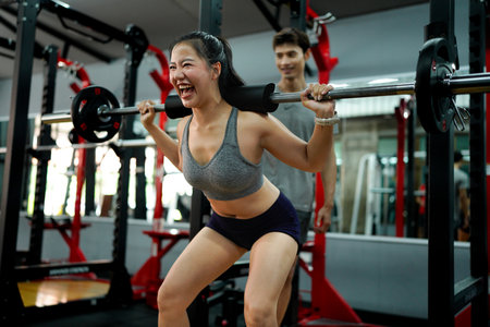 Professional fitness trainer guiding female athlete performing precise barbell squats in modern gym setting. Motivation and healthy lifestyle concept.の写真素材