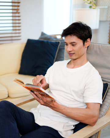 man relaxing at the armchair at home while reading his favorite book.