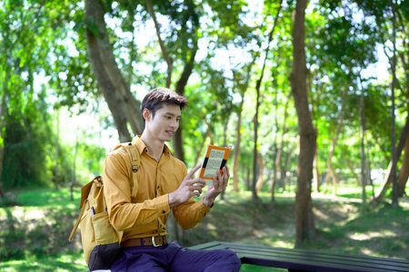 young man enjoying leisure time on a park bench, reading a book and drinking coffee on a sunny day...