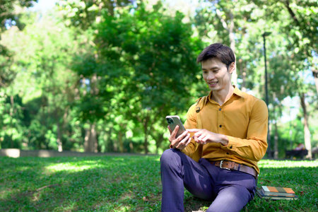 Young asian businessman using smartphone outdoors in park.