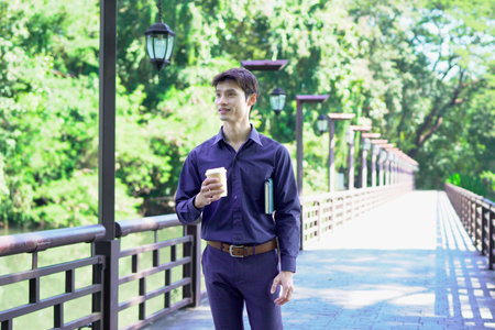 Man holding coffee cup or disposable cup with coffee and book standing in the garden green nature background. Concept happy people with leisure and drink coffee..の写真素材