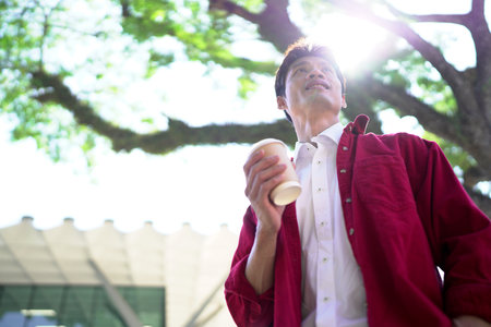 Young man standing on urban city center street, drinking coffee to go. Town lifestyles outside..の写真素材