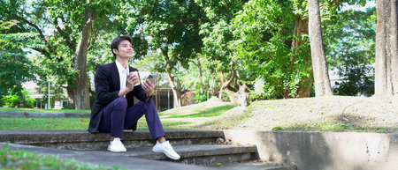 Smiling businessman using smartphone and holding coffee outside.の写真素材