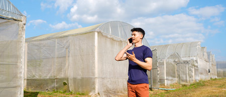 Portrait of a farmer in front of a greenhouse talking on a mobile phone.