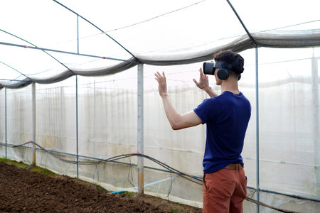 Young asian man smart farmer standing in greenhouse and wearing visual reality glasses technology..