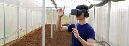 Young asian man smart farmer standing in greenhouse and wearing visual reality glasses technology..