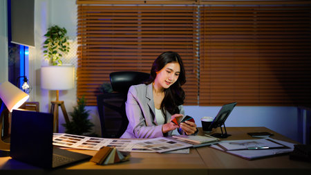 Interior Designer at Work: Asian Adult Woman Choosing material samples and color swatches for Home Renovation Project with Architectural Plans on Desk at night.の写真素材