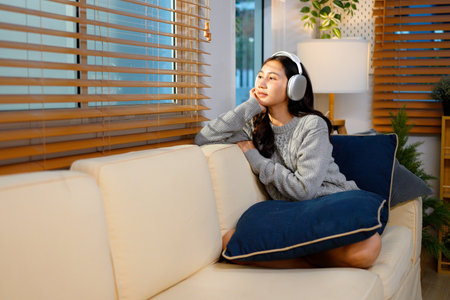 Young asian woman with headphones relaxing at home. listening to music. sitting on cozy sofa wearing headphone.の写真素材