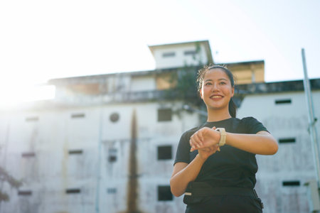 Smiling sporty woman checking smartwatch after exercising outdoors in a park.の写真素材