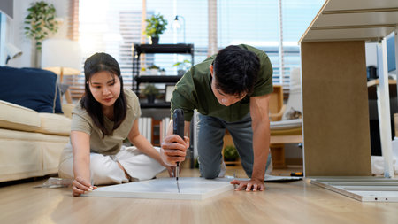 Asian adult couple assembling wooden furniture together in modern living room create new home decor DIY project happiness.の写真素材