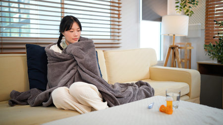 Sick, woman in home for virus infection, influenza or allergy on living room sofa. Girl, winter and fever with high temperature in lounge, cold or medical health problem with blanket.の写真素材