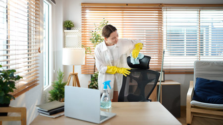Housekeeper doing chores, young woman in yellow rubber gloves wipe a chair with a blue cloth and a...