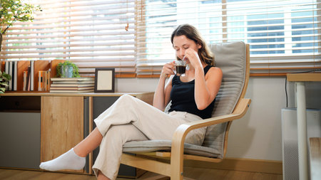 Happy caucasian woman relaxing drinking hot coffee or tea in holiday morning vacation on armchair at...