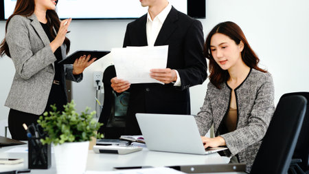 Focused female manager reading e-mails over laptop while colleagues working in the background in...