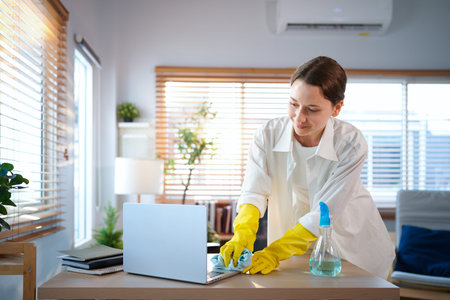 woman in gloves cleaning and wiping laptop computer with disinfectant.