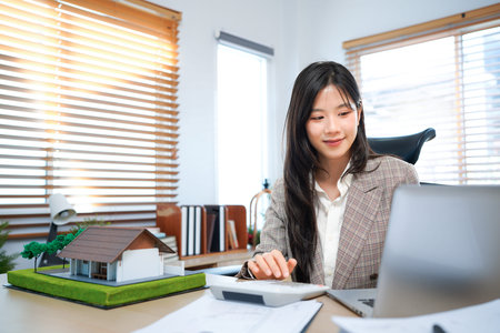 Business mortgage realtor with house model, sitting at desk, real estate agent manager working on...