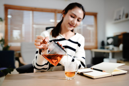 woman work take break in job pouring hot tea from transparent kettle into cup, female prepare tea at...