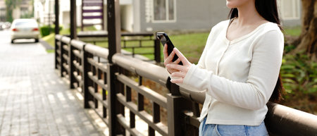 Close up hand Teenage girl using smartphone in a city. Student girl texting on mobile phone outdoor....