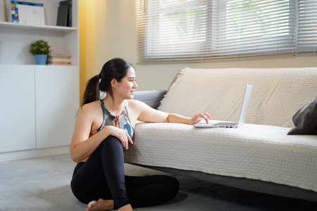 woman in sportswear sitting on floor with laptop on couch scrolling for best training tutorial for...