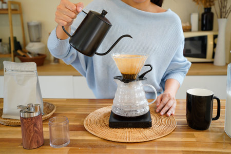 Young asian woman pouring hot water from black kettle into coffee dripper, Female brewing drip...