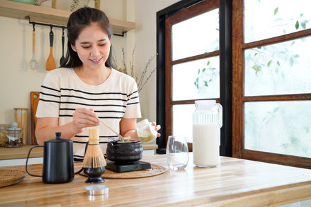 Young Asian woman carefully scooping matcha powder into a traditional tea bowl in a calm and...