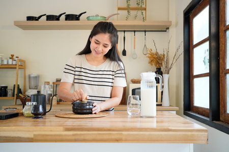 Young Asian woman making traditional matcha tea at home, whisking green tea powder in a bowl with a...