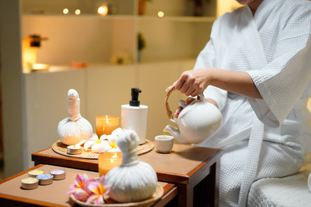 Beautiful young woman in white robe relaxing after spa procedures in oriental spa resort, drinking...