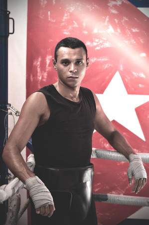 Portrait of sweaty latin american male boxer leaning on ropes on a boxing ring.の写真素材