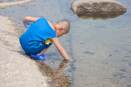 Small boy picking aquatic weed near the stream のeditorial素材