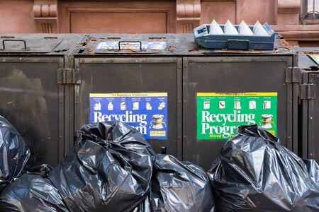 New York City, USA - July 1, 2019: old rusty recycling program trash with black plastic trash bagsの写真素材