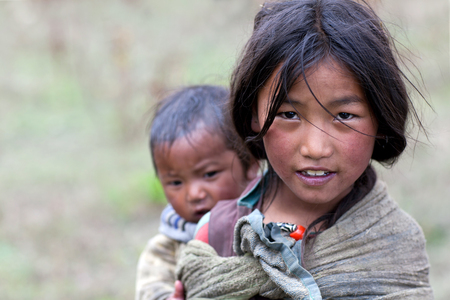 DHO TARAP, NEPAL - SEPTEMBER 10: Tibetan girl with her baby brother walkig on the road on September 10, 2011 in Dho Tarap village, Upper Dolpo, Nepalのeditorial素材