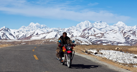 NGARI, TIBET - APRIL 26, 2013: Nomad on motorbike riding down on a National highway in Ngari Prefecture, Western Tibetのeditorial素材