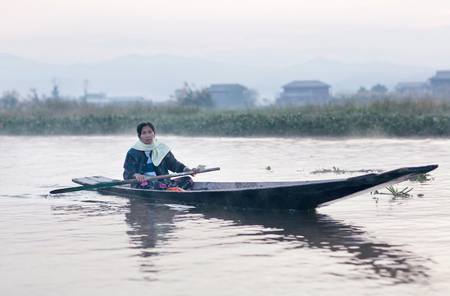 NYAUNG SHWE, MYANMAR - JANUARY 12, 2012: Intha woman sailing in wooden boat on Inle lake in Shan State, Myanmarのeditorial素材