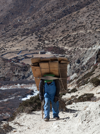 DINGBOCHE, NEPAL - JANUARY 13, 2017: Nepalese porter carrying a heavy load to the pass in Sagarmatha National Park, Himalayasのeditorial素材
