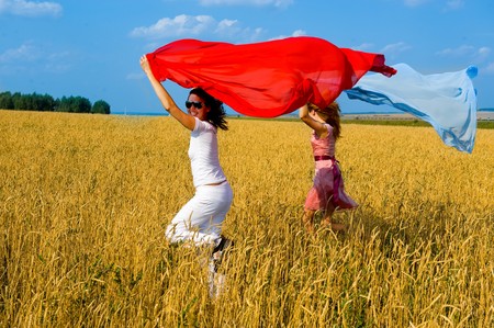 Two young beautiful woman running on the field with a red and blue scarfsの写真素材
