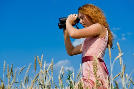 Search. Woman looking through binoculars with a blue sky as backgroundの写真素材