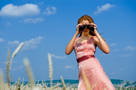Search. Woman looking through binoculars with a blue sky as backgroundの写真素材