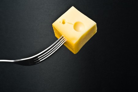 Metallic fork with slice of cheese on black backgroundの写真素材