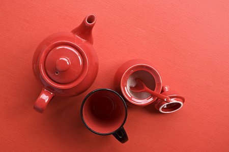 Teapot, cup and sugar bowl with spoon on red tableの写真素材