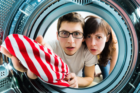 Funny couple loading clothes to washing machine. From inside the washing machine viewの写真素材
