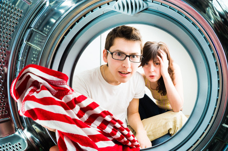 Funny couple loading clothes to washing machine. From inside the washing machine viewの写真素材