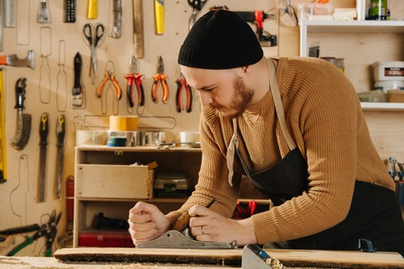 Portrait of working carpenter. He is making furniture on order in a workshop. Leveling surface with jointer. Creating desired piece.の写真素材